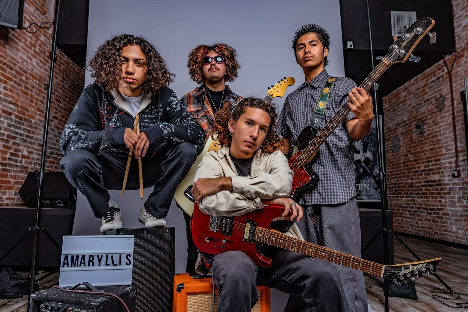 Band members holding guitars pose against brick wall in studio during photoshoot.