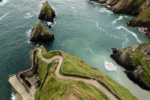 Winding coastal road curves along dramatic cliffs overlooking turquoise waters at Dunquin Harbor in Ireland.