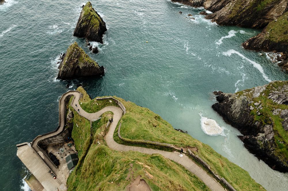 Winding coastal road curves along dramatic cliffs overlooking turquoise waters at Dunquin Harbor in Ireland.