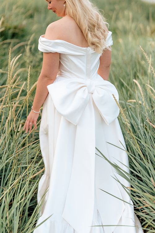 Details of an elegant white wedding gown with a large bow accent photographed among tall grass in multiple angles.