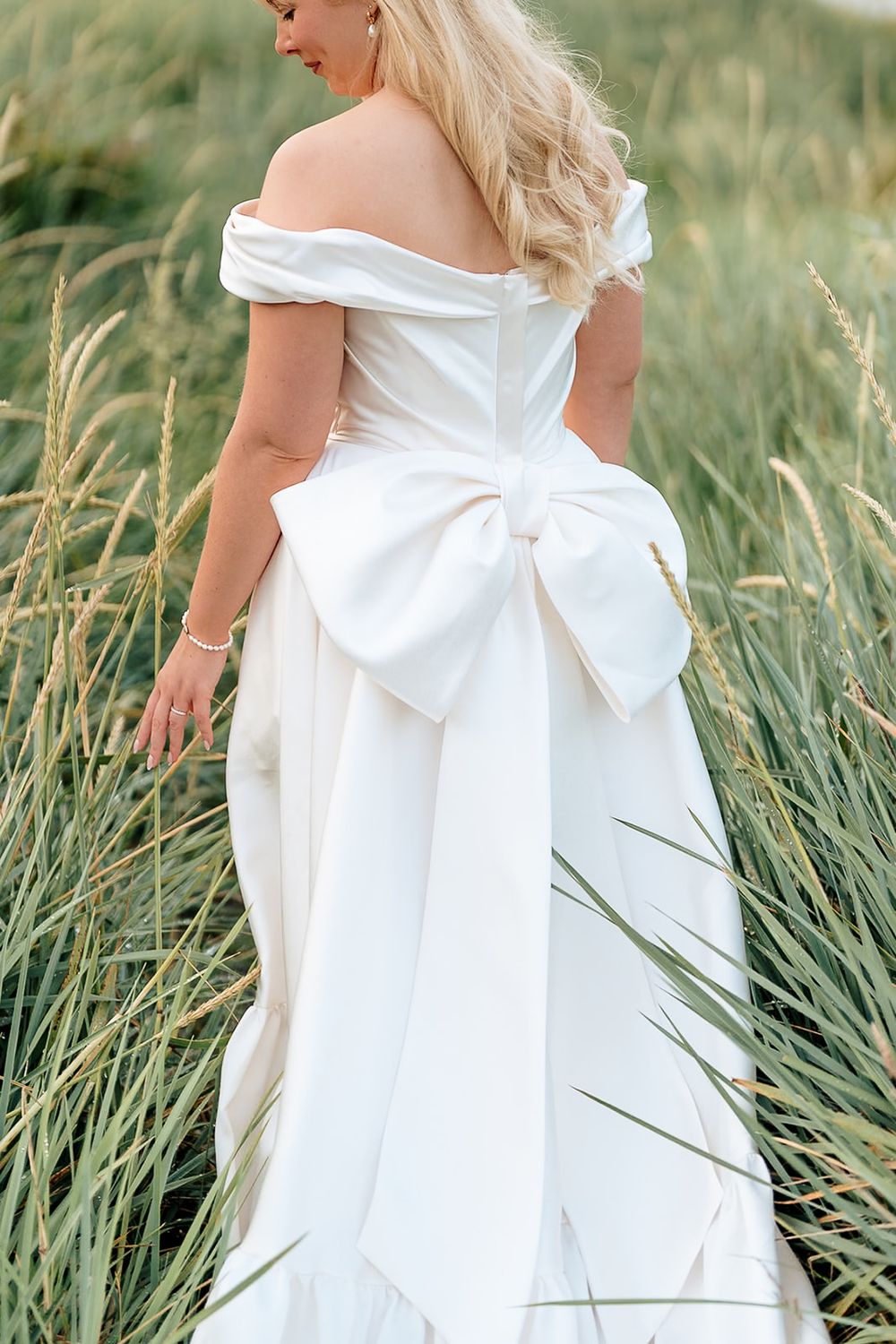 Details of an elegant white wedding gown with a large bow accent photographed among tall grass in multiple angles.