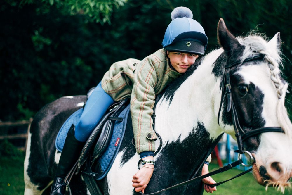 A black and white horse with riding gear stands in a grassy field.