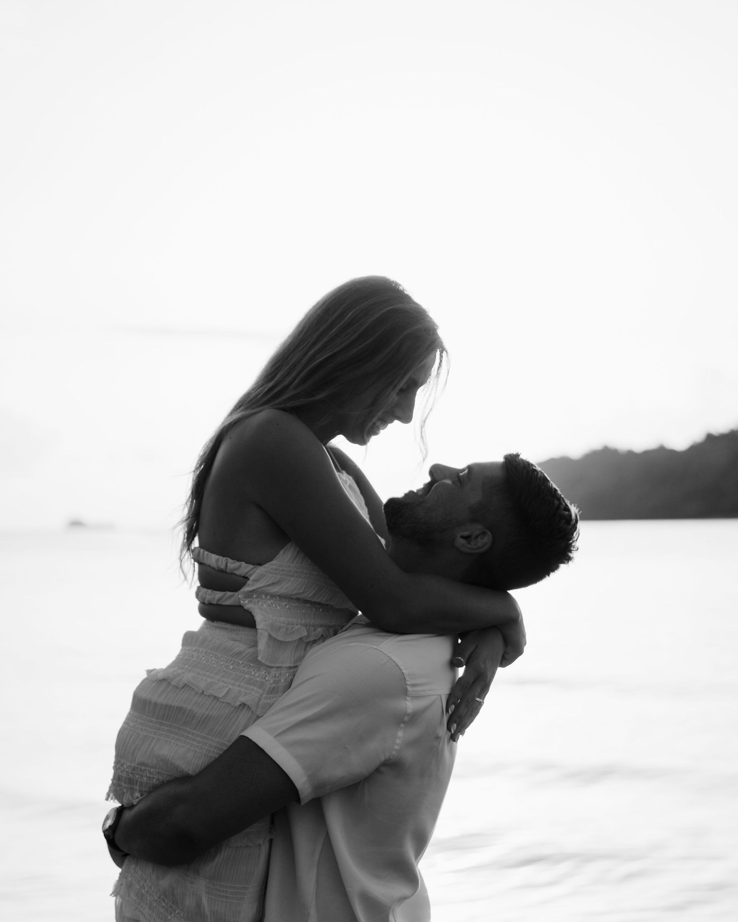 A romantic black and white photo of a couple embracing on a beach at sunset.