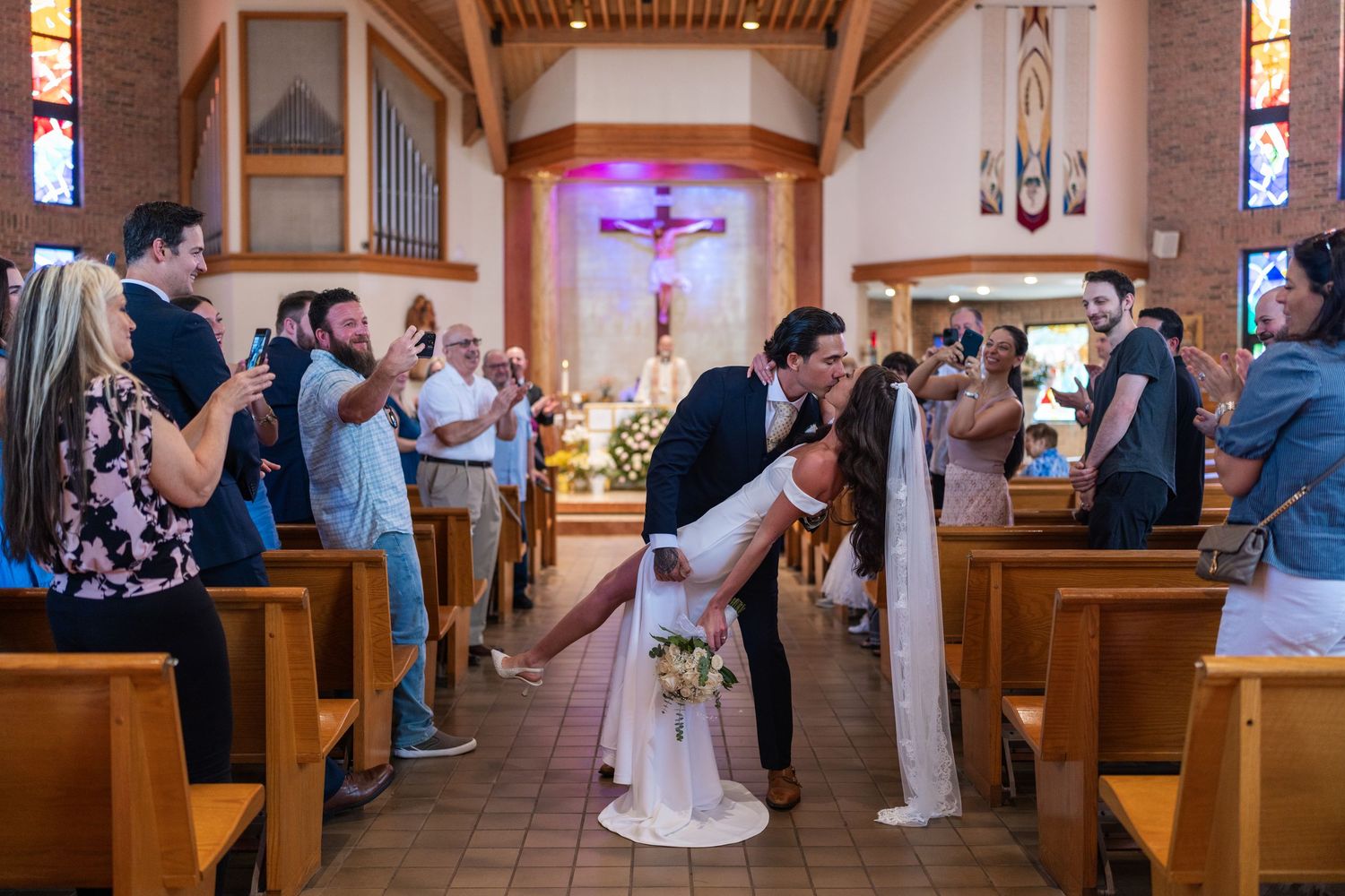 Wedding ceremony in progress inside a traditional church with wooden pews and stained glass windows.
