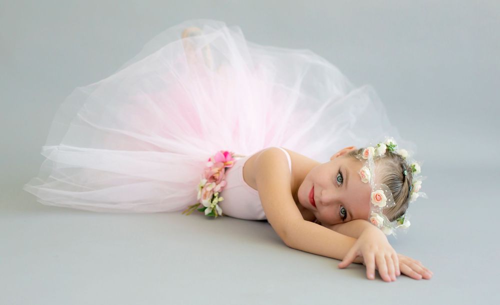 Young ballet dancer in pink tutu lying gracefully on floor.