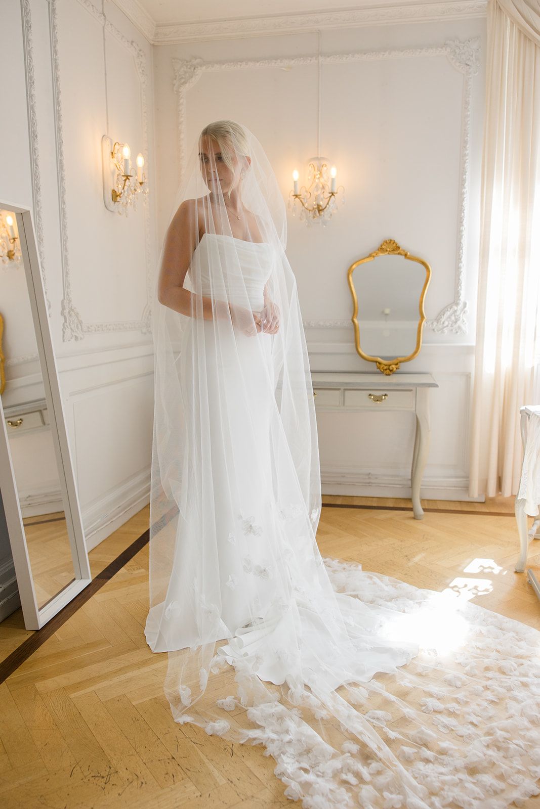 Elegant bridal portrait in a white room with chandelier featuring a long flowing veil.