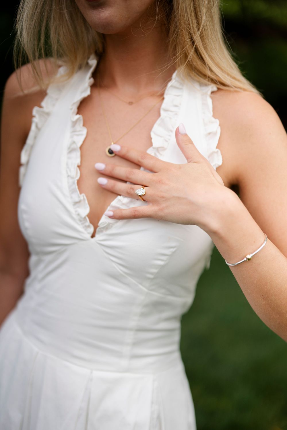 Close-up of bride in white ruffled halter wedding dress showcasing engagement ring and delicate bracelet.