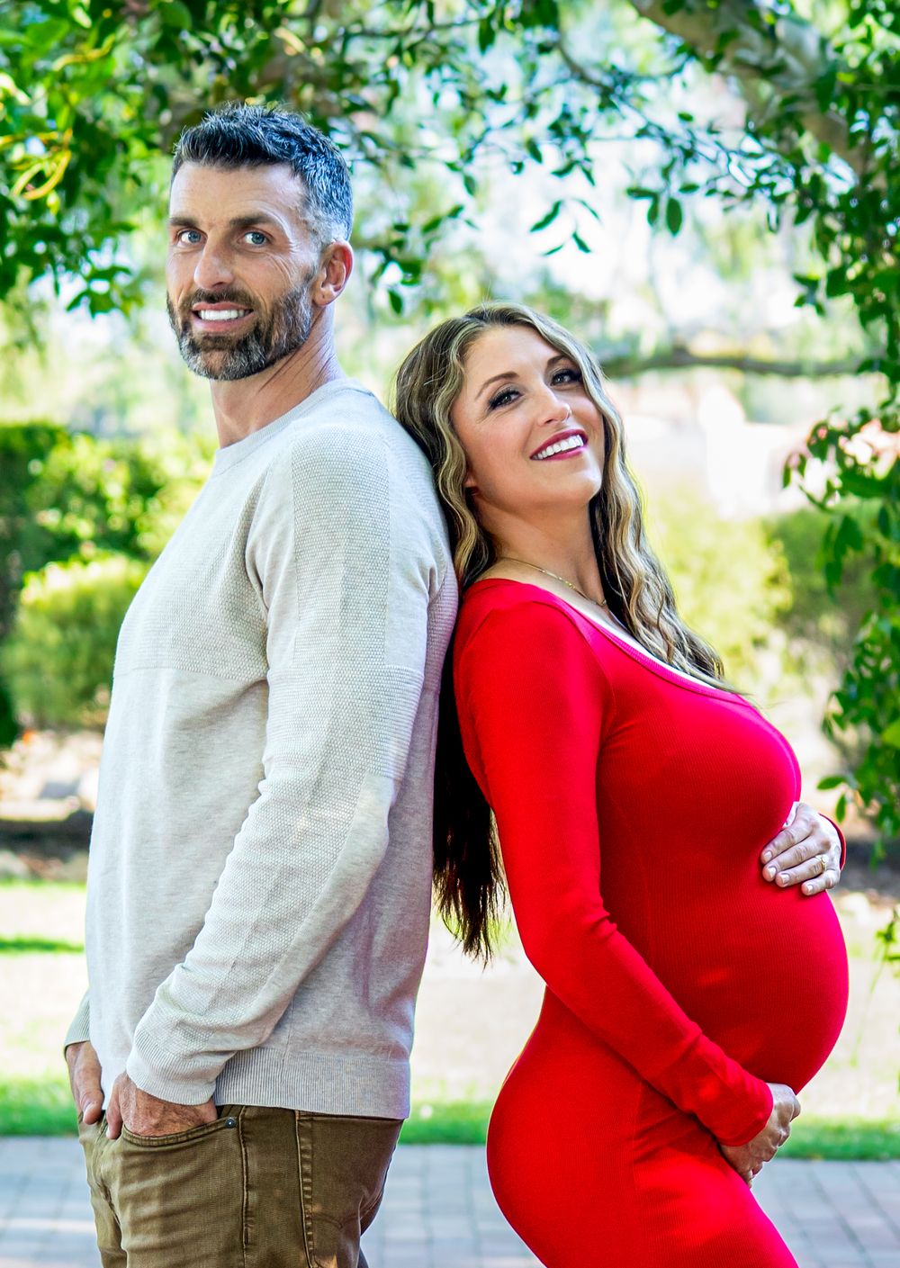 Joyful maternity photography session in a sunlit garden with a red dress.