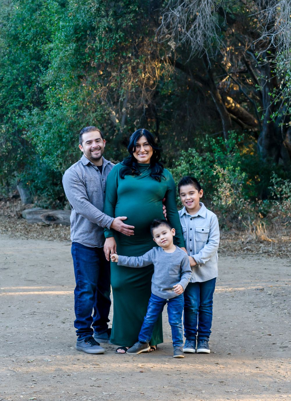 A family stands together on a dirt path surrounded by green trees and foliage on a sunny day.