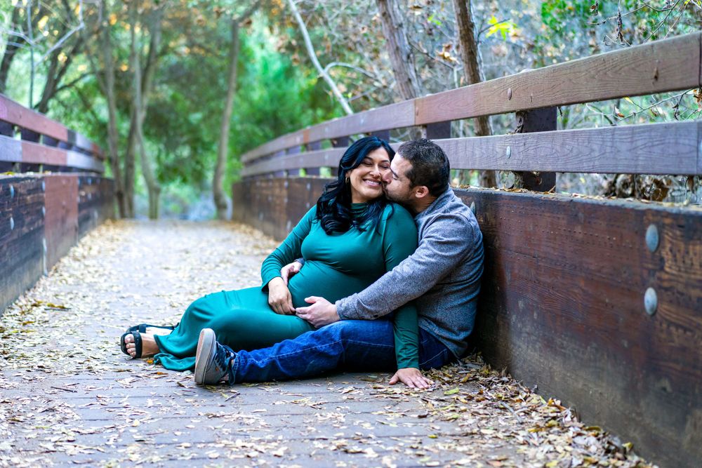 A couple sits together on a wooden bench along a peaceful wooded walking trail.