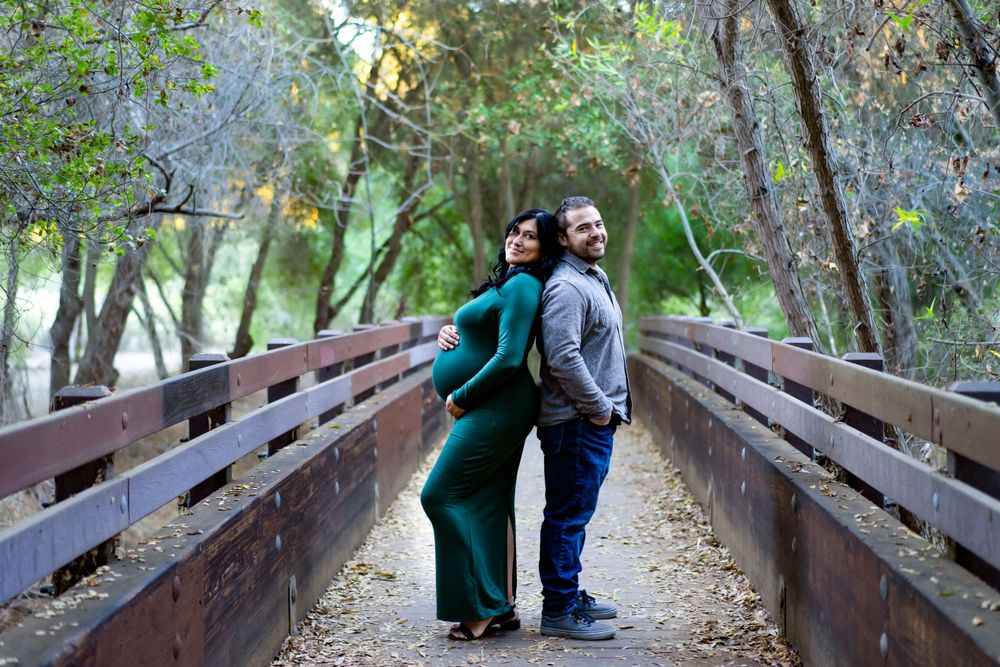A couple share a romantic moment on a rustic wooden bridge surrounded by lush green forest scenery.