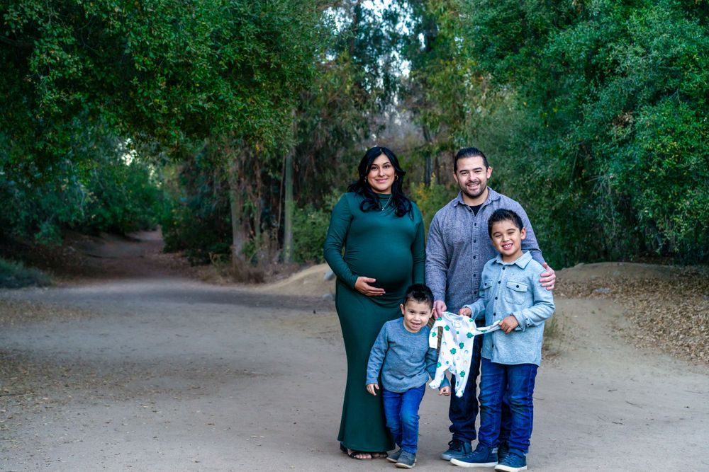 A family stands together on a tree-lined path in a park during their outdoor portrait session.