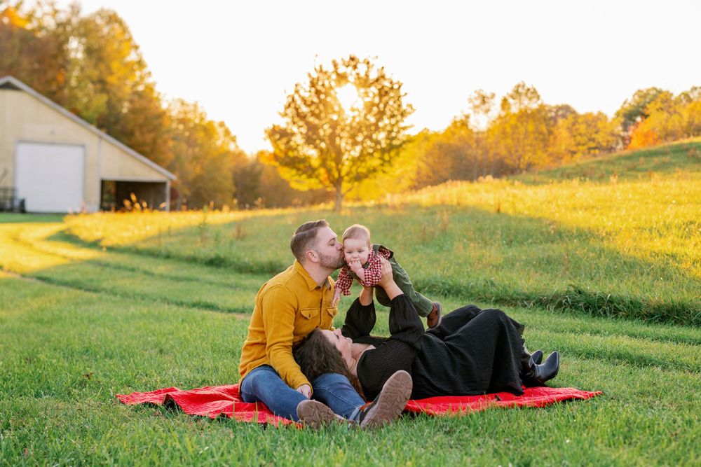 Couple relaxing on red blanket in sunny field during golden hour.