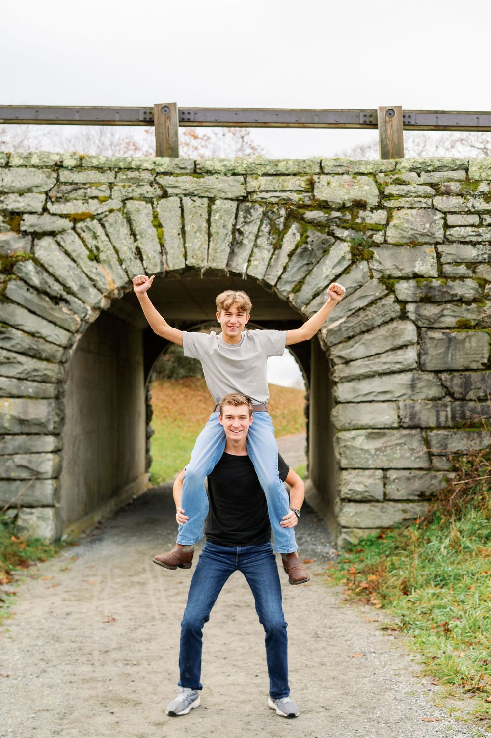 Two people having fun posing under a stone archway tunnel outdoors.