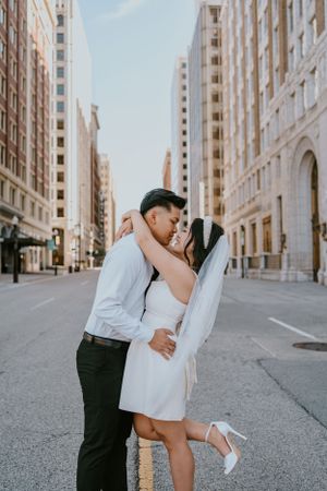 A romantic couple embraces for a kiss in the middle of a city street with tall buildings.