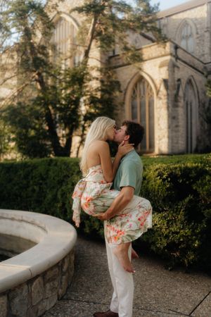 A romantic couple embraces near a stone church building during a sun-drenched outdoor photoshoot.