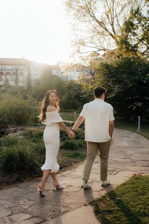 A couple holds hands while walking along a stone path during a sunset engagement session.