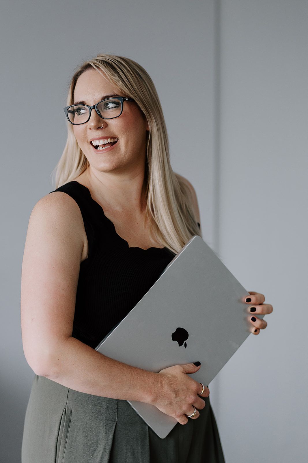 Professional portrait of someone wearing glasses and a black sweater leaning on a white chair.