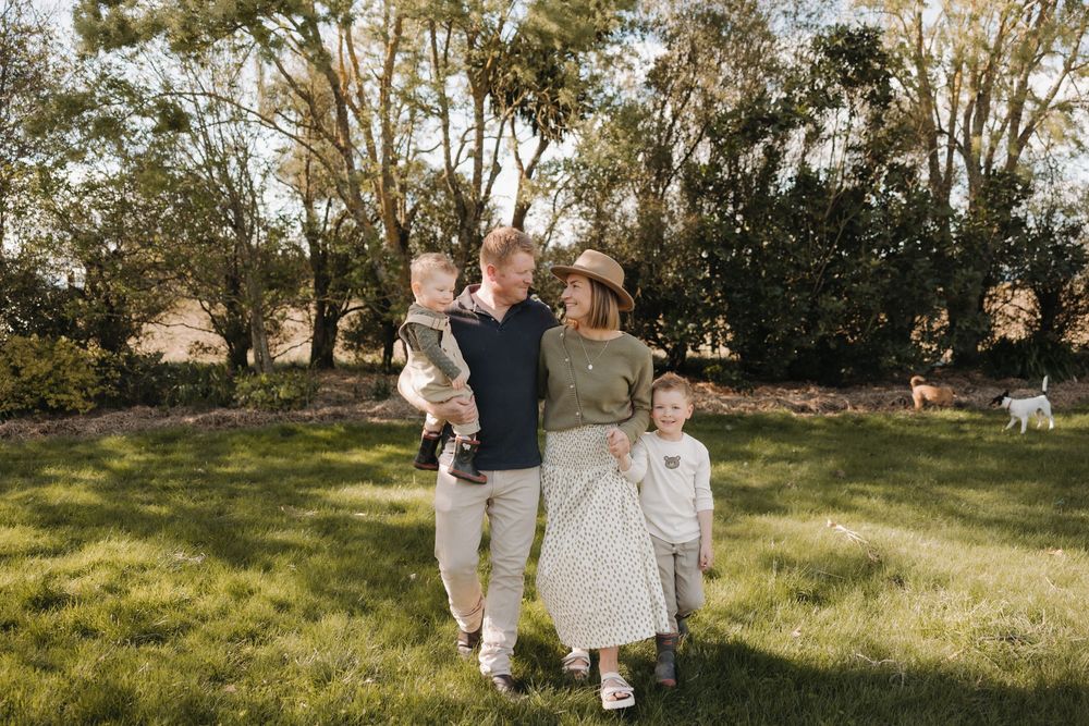 A family poses together in golden sunlight on a grassy hillside.