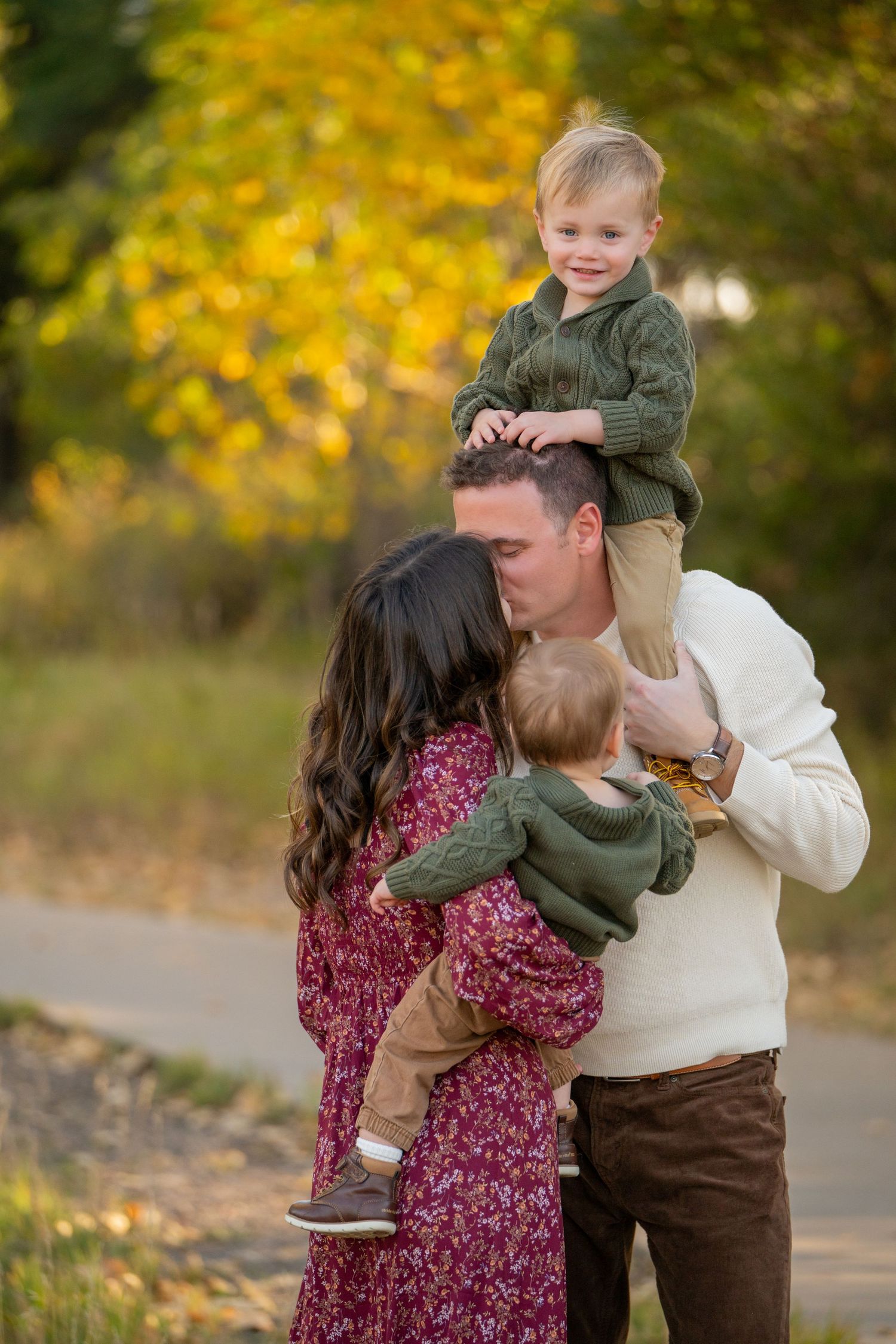A family shares an affectionate moment outdoors during autumn with golden yellow foliage in the background.