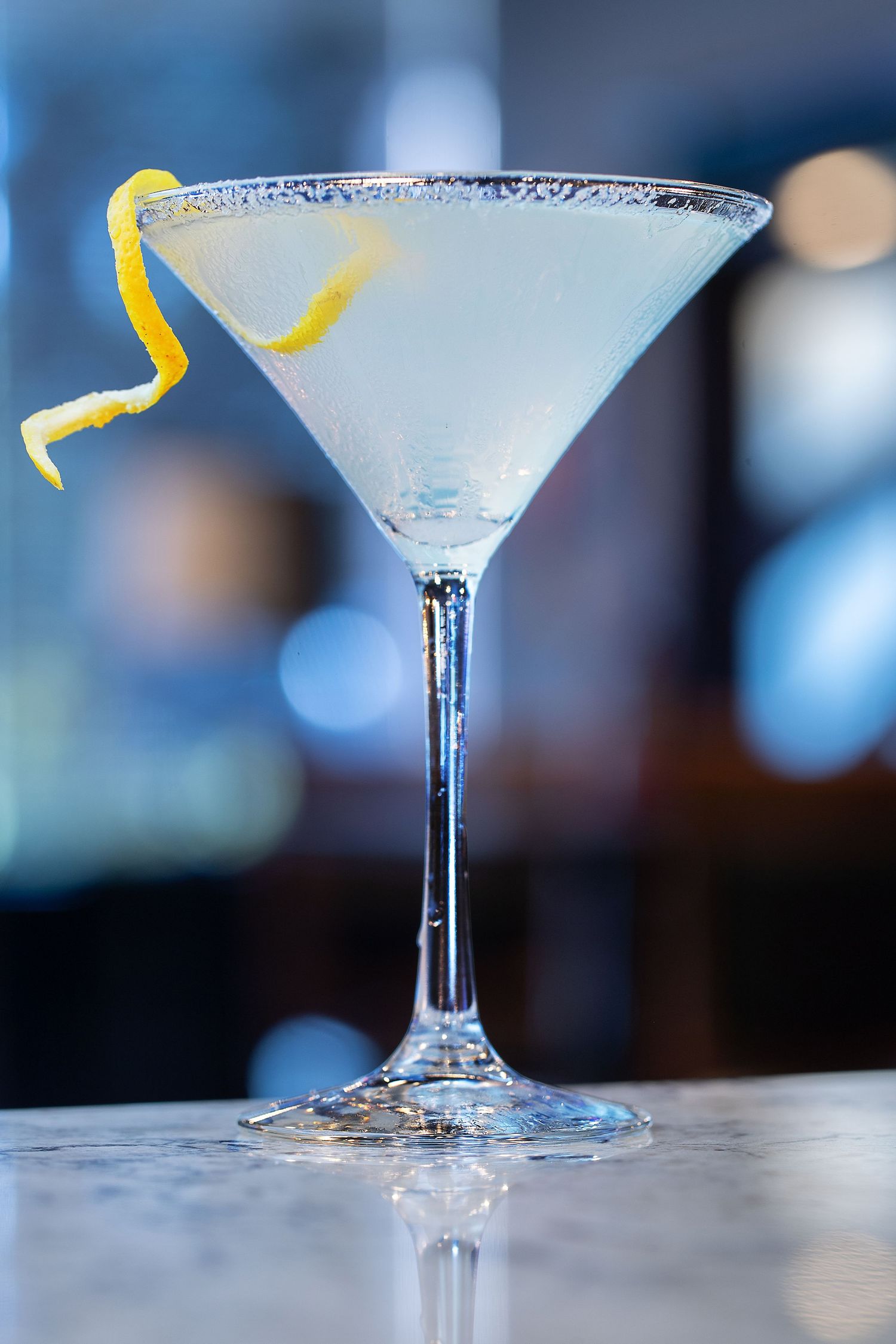 Elegant martini glass with frosted rim and lemon twist garnish on a bar counter.