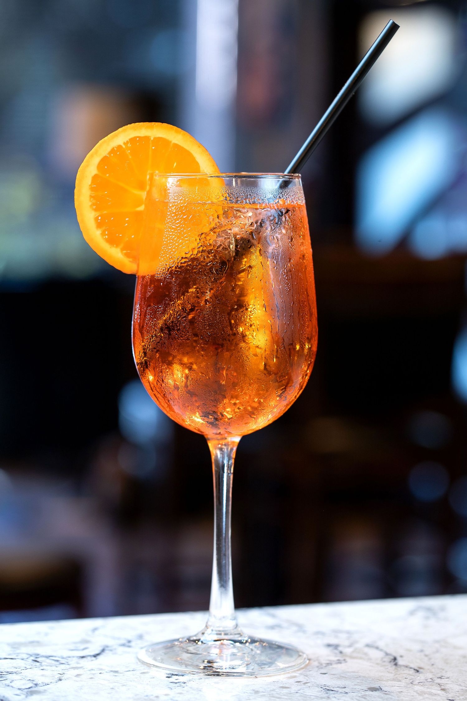 Orange cocktails in wine glasses garnished with citrus slices on a marble bar counter.