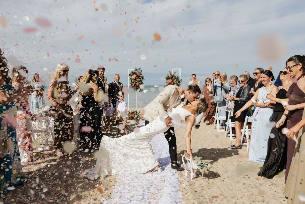 Wedding guests toss biodegradable confetti during aisle exit beach wedding with a dip kiss photo at The Baths Wedding in Sorrento