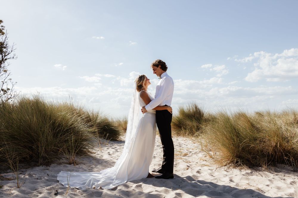 Couple embracing among coastal sand dunes on a bright, sunny day.
