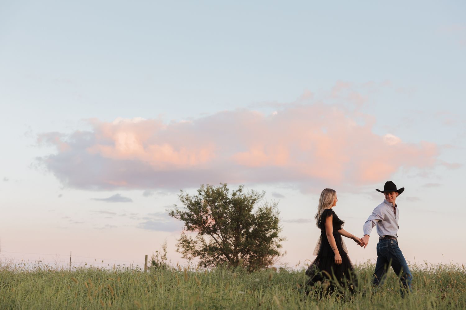 People embrace in a romantic moment on a hilltop at sunset with cotton candy clouds in the background.
