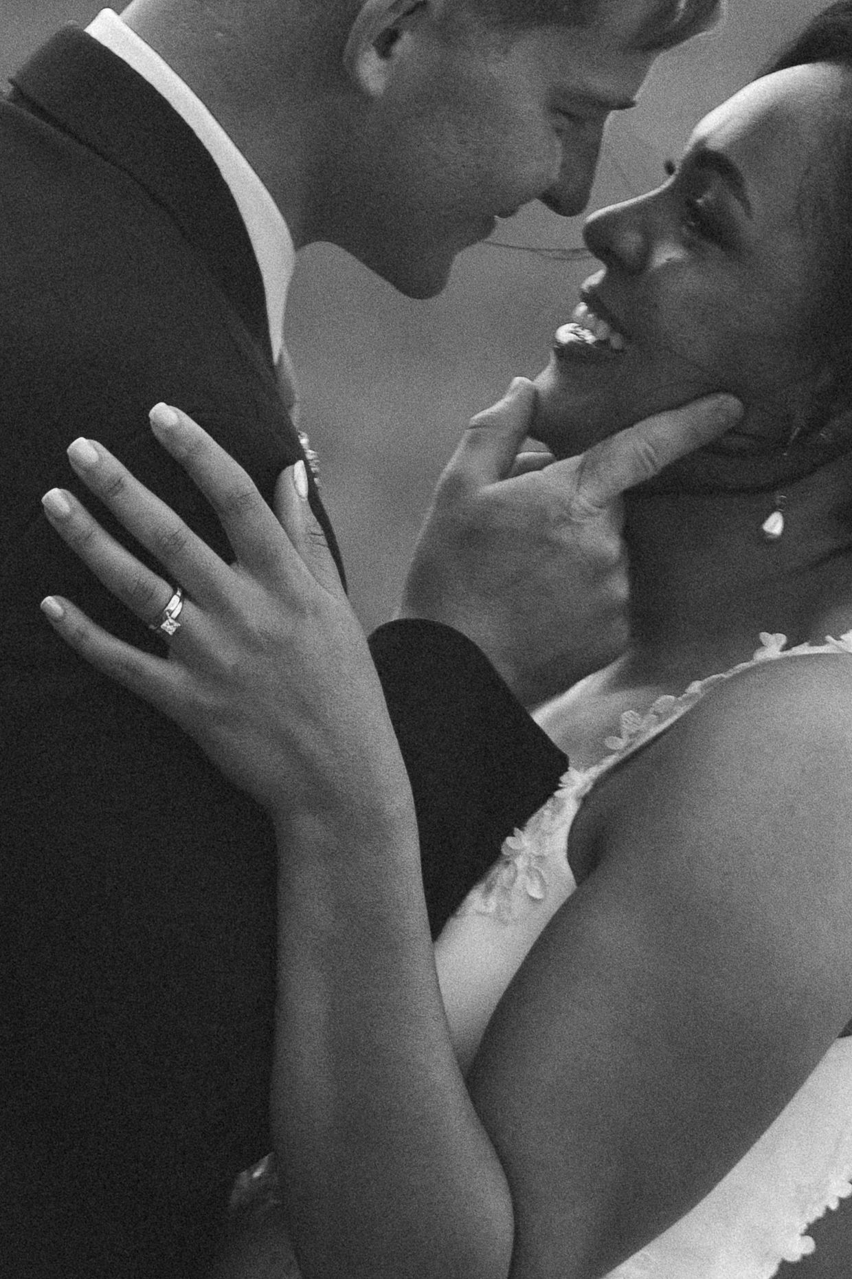 Black and white wedding photo of bride and groom sharing a romantic moment, with visible wedding ring on her hand.