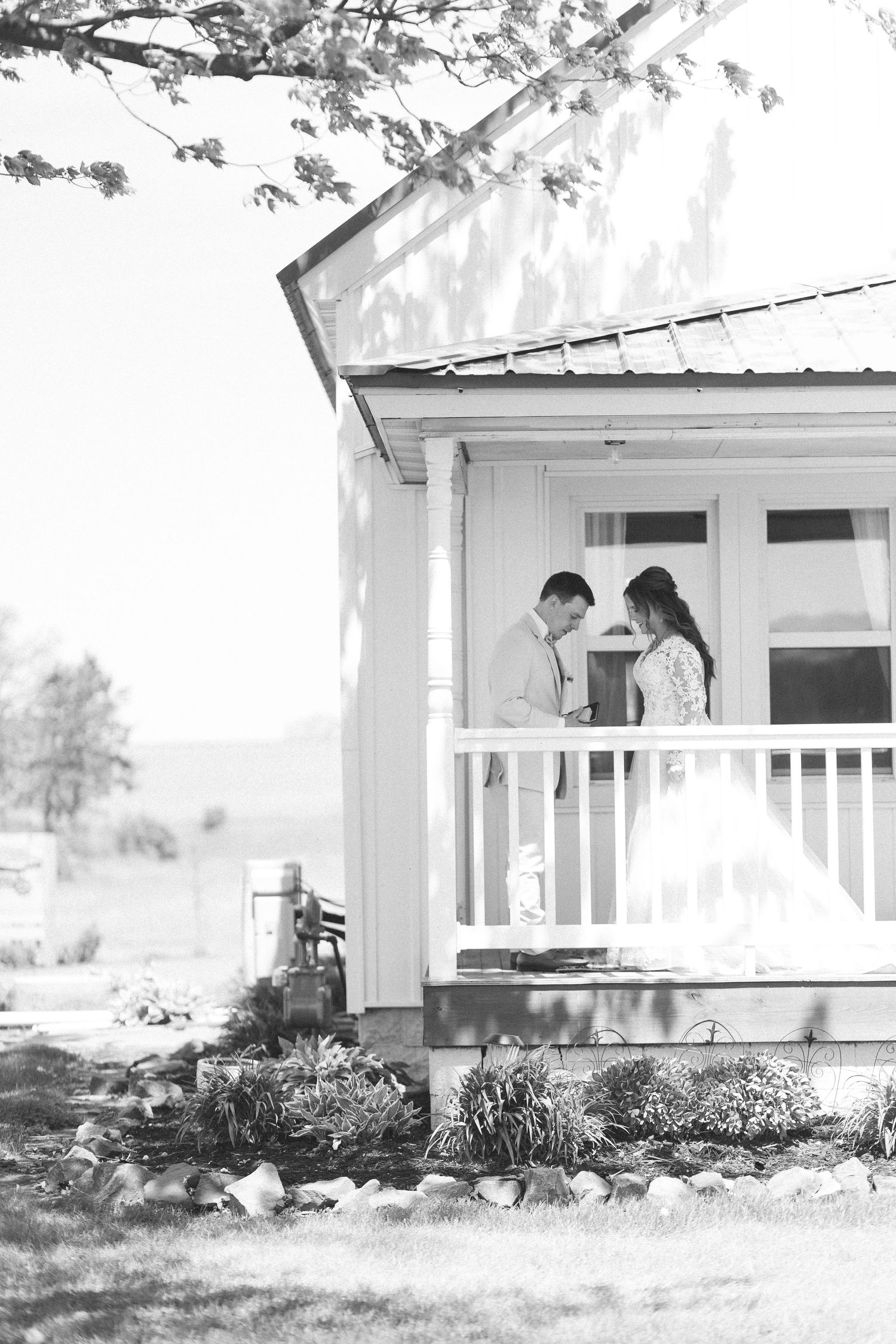 Black and white photo of a bride and groom sharing a tender moment on a charming cottage porch on their wedding day.