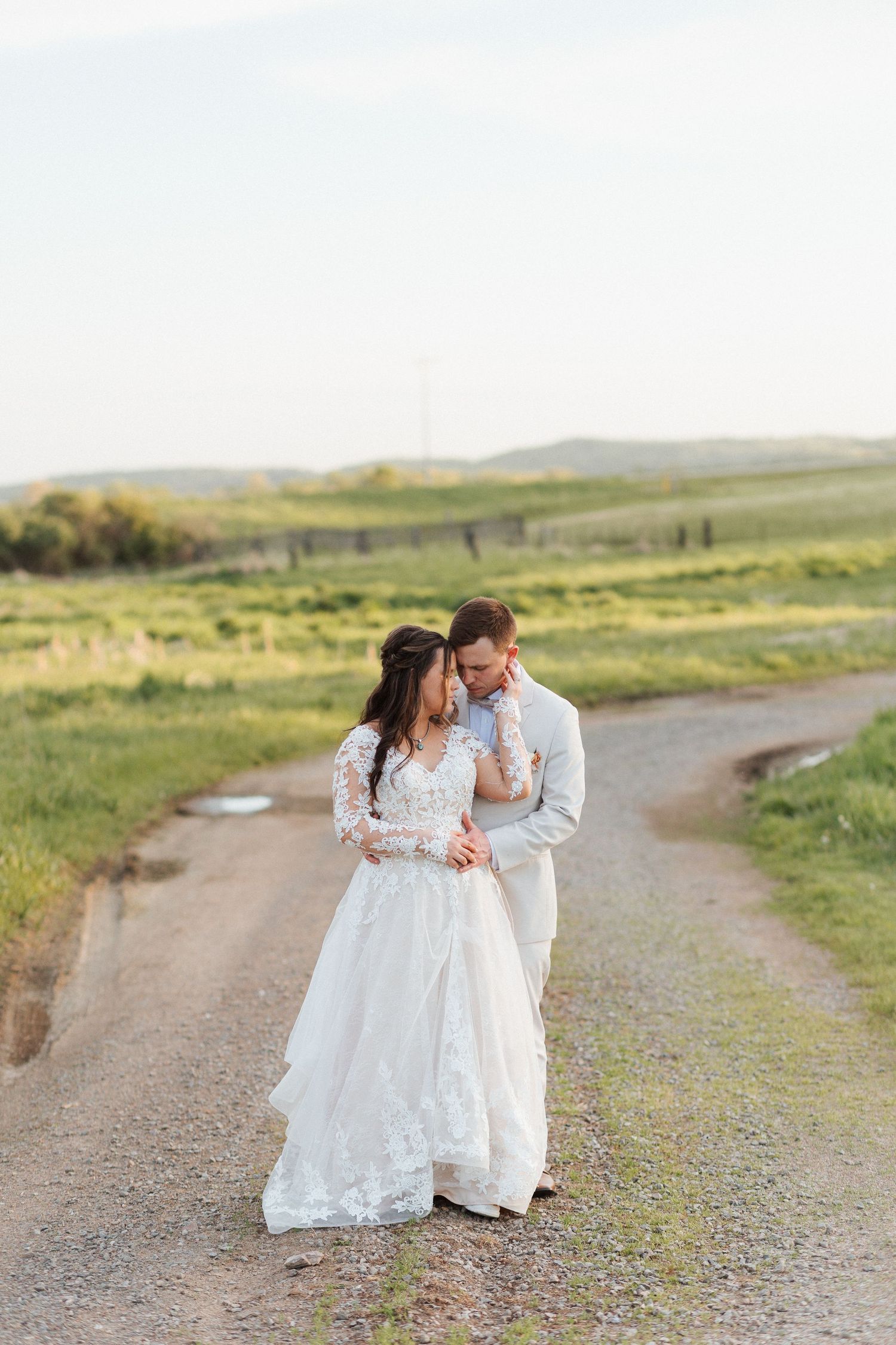 Bride and groom walking on a dirt path through green fields during golden hour wedding photography.