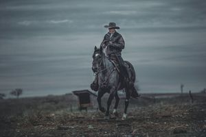 A cinematic western scene shows a rider on horseback silhouetted against a moody, overcast sky.