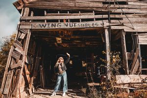A person explores an abandoned wooden barn with rustic beams and weathered walls in warm sunlight.