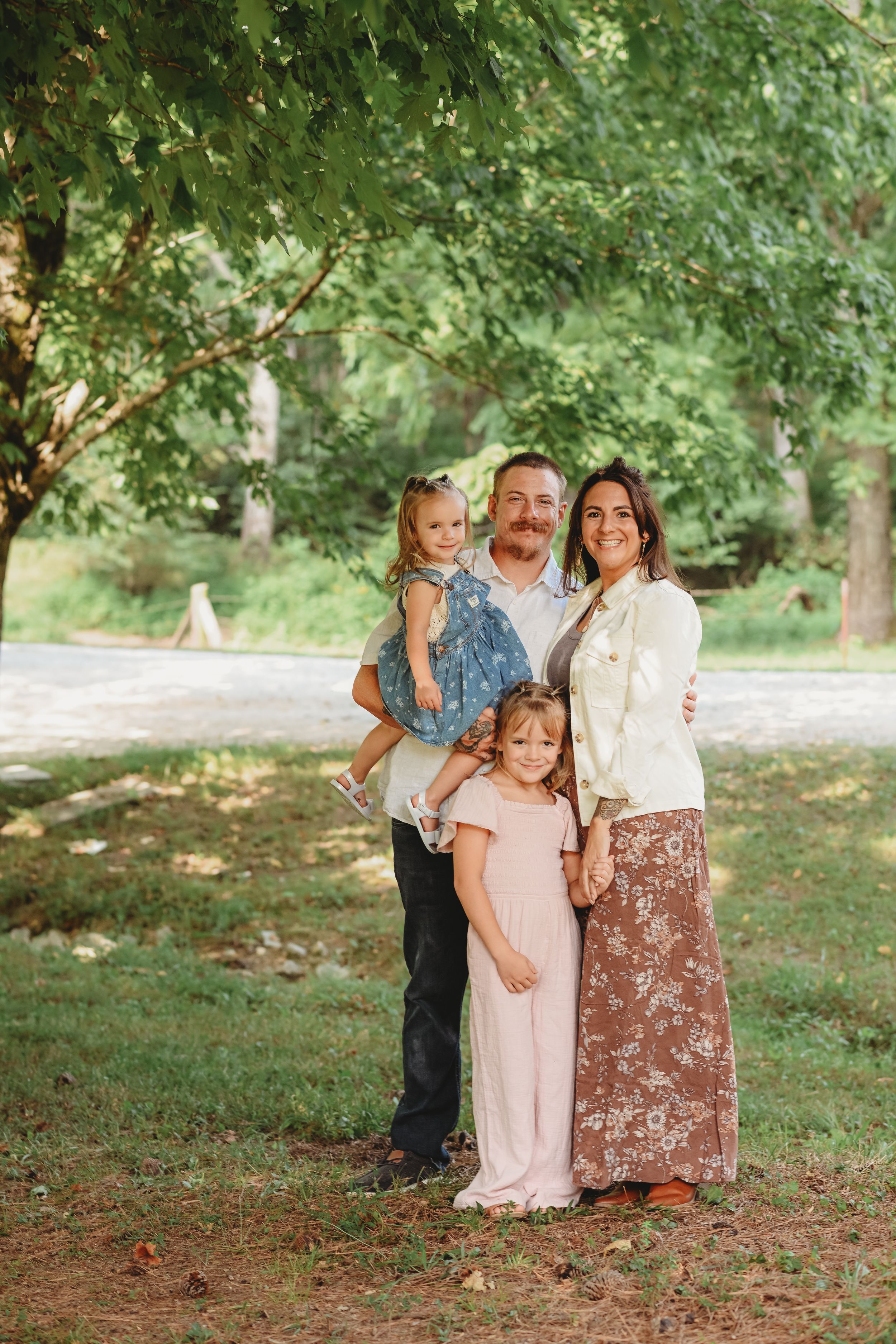 Family portrait under green trees in a park setting.