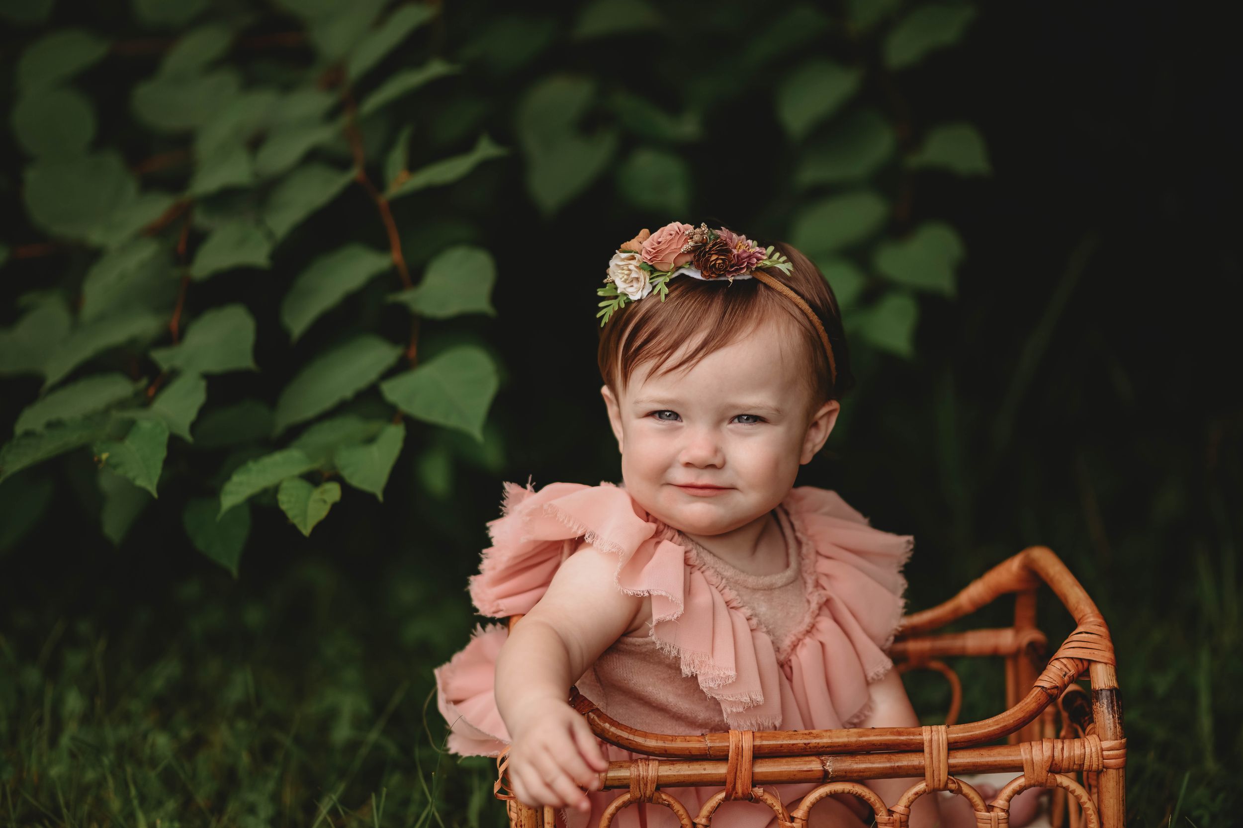 Baby in a peach-colored ruffled dress sits on vintage lace blanket in outdoor garden setting.