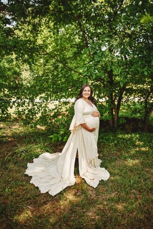 Ethereal maternity portraits with flowing cream dress in wooded natural setting.