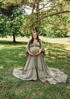 A flowing sage green vintage-style dress spreads across grass in a dreamy outdoor setting.