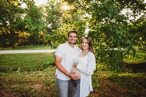 Maternity photoshoot in natural outdoor setting with soft evening light filtering through trees.