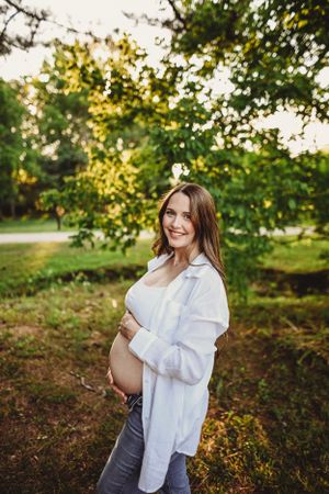 Candid maternity portraits captured in a wooded setting during sunset.