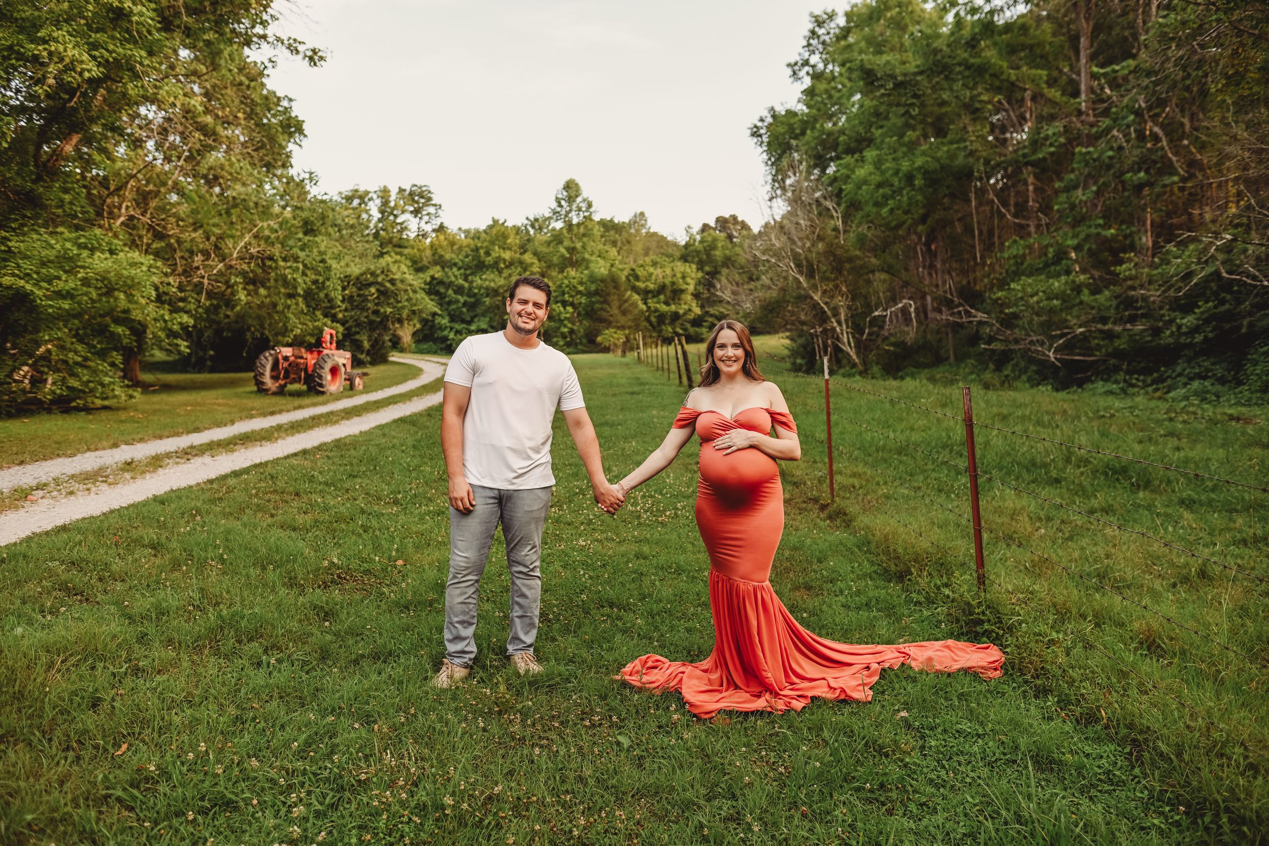 Dramatic maternity photos with flowing red dress in pastoral setting at sunset.