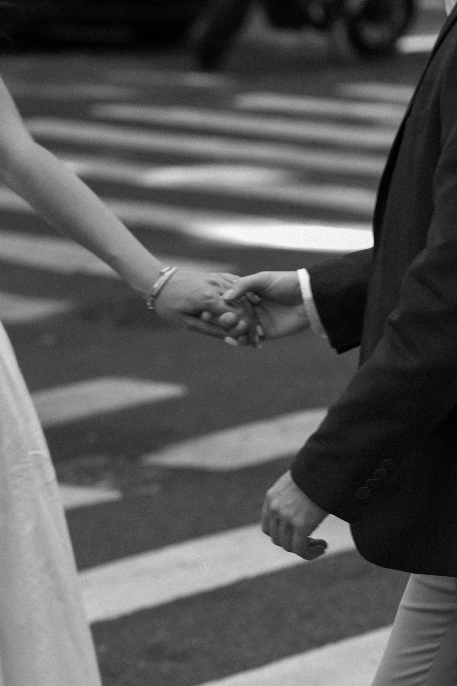 Black and white close-up of newlyweds holding hands with wedding attire visible.