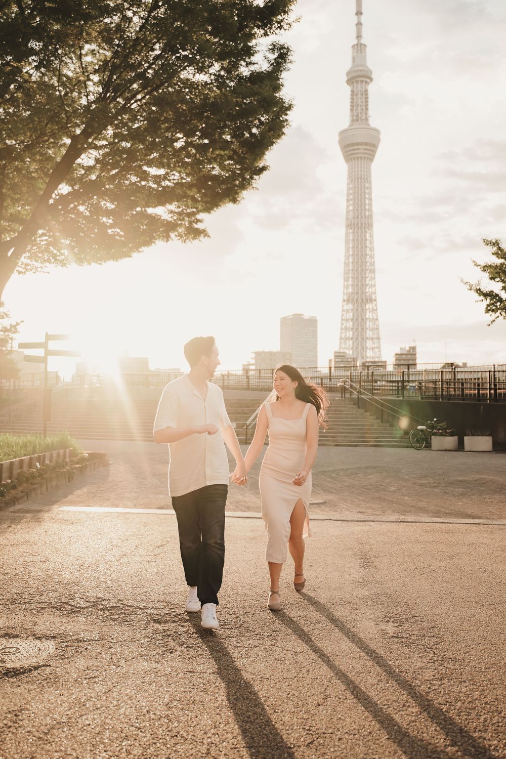 Couple holding hands walking at sunset with Tokyo Skytree in background.