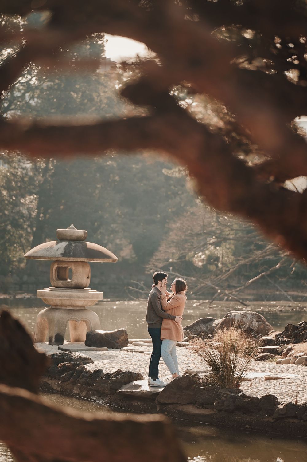Couple embracing near a stone lantern in a serene Japanese garden, framed by autumn tree branches.
