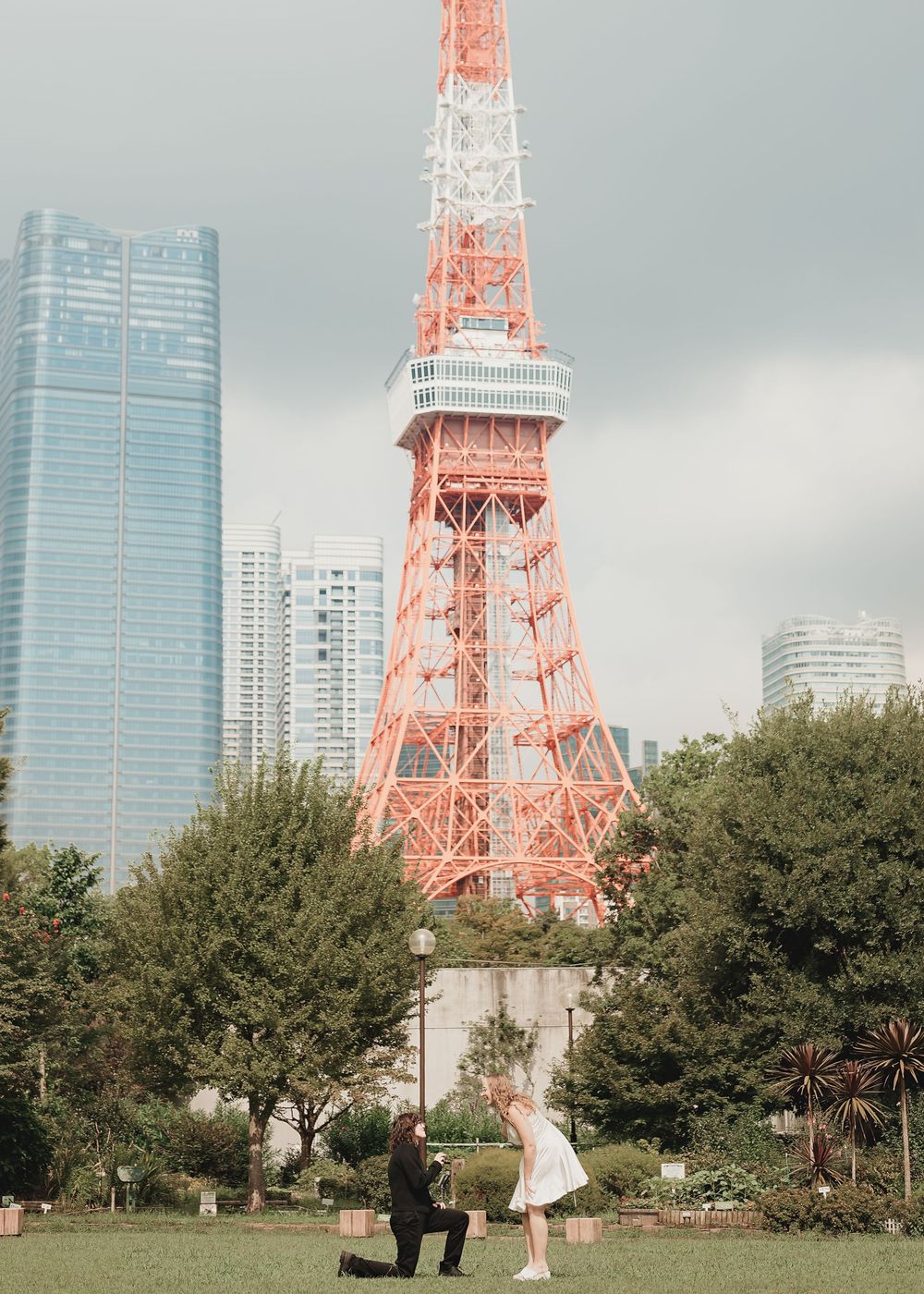 A couple shares a marriage proposal moment in front of Tokyo Tower with city skyline backdrop.