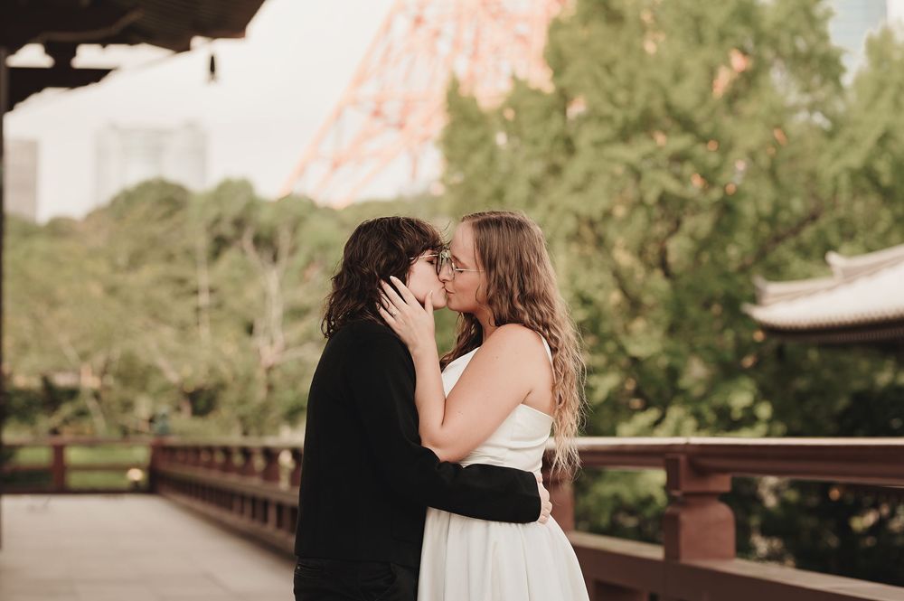 Couple sharing a romantic kiss in front of Tokyo Tower, bride in white dress and groom in black suit.