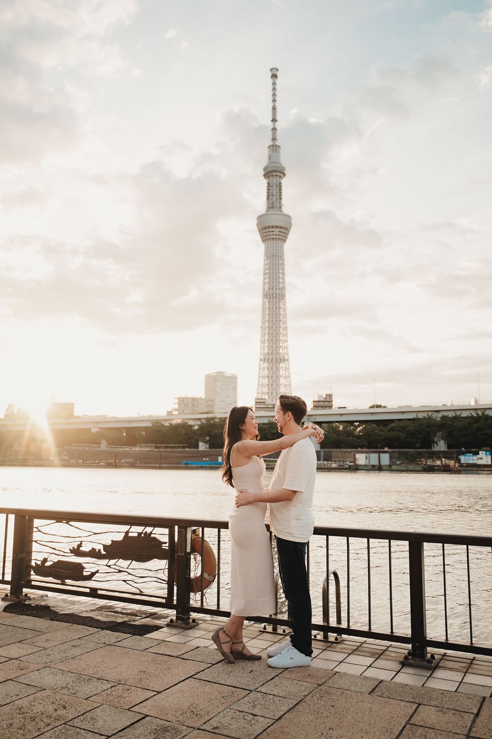Couple embracing by the waterfront with Tokyo Skytree tower at golden sunset.