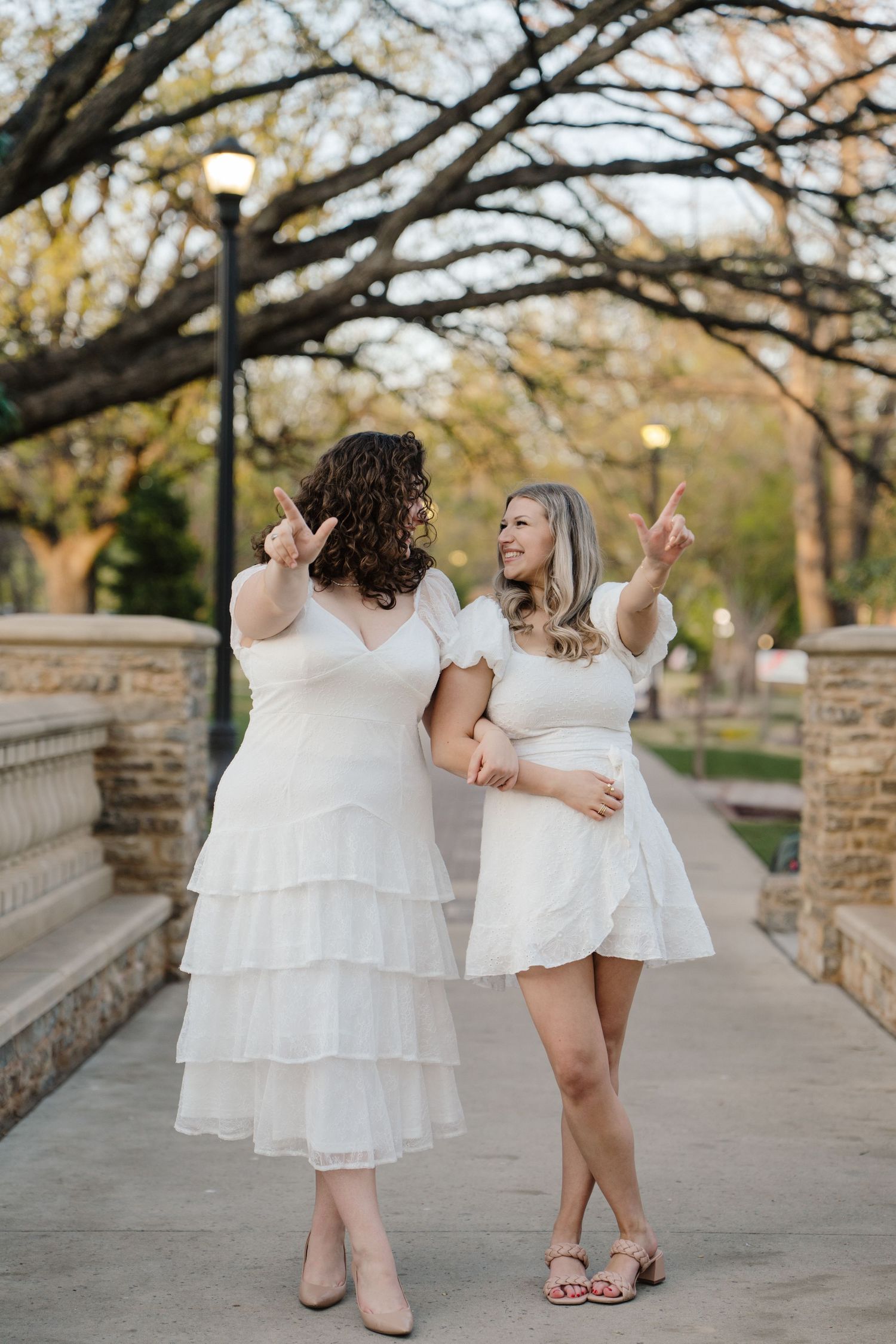 Two people in white dresses share a playful moment on a stone bridge pathway.