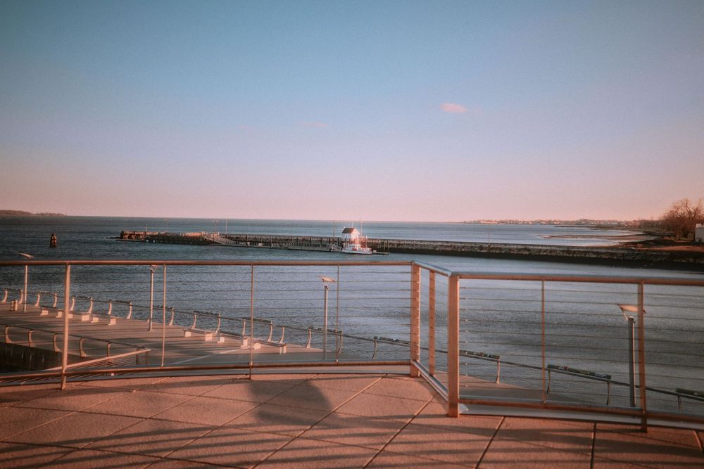 Sunset view of a waterfront deck with metal railings overlooking a calm harbor.