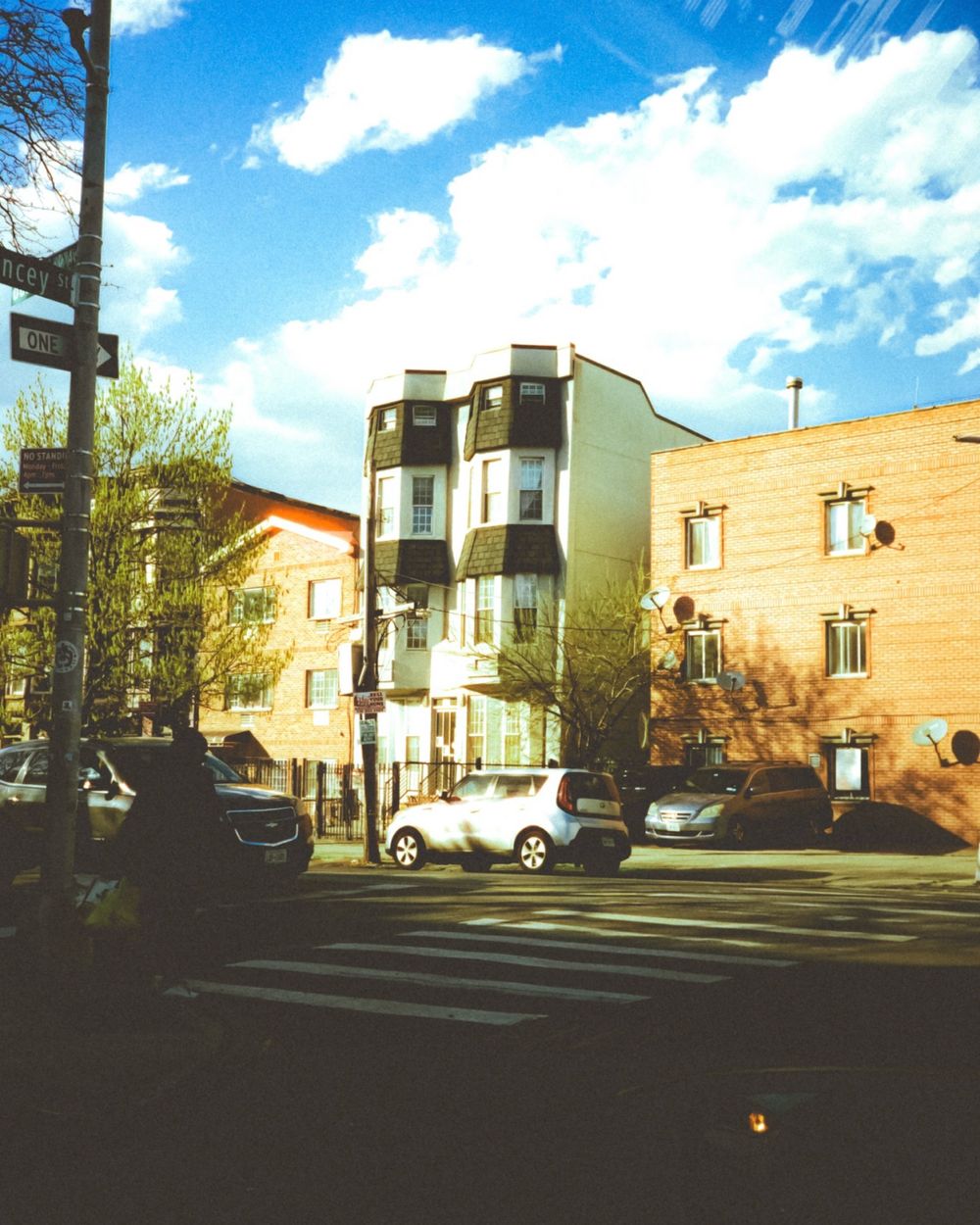 A multi-story apartment building with bay windows on a sunny residential street corner.